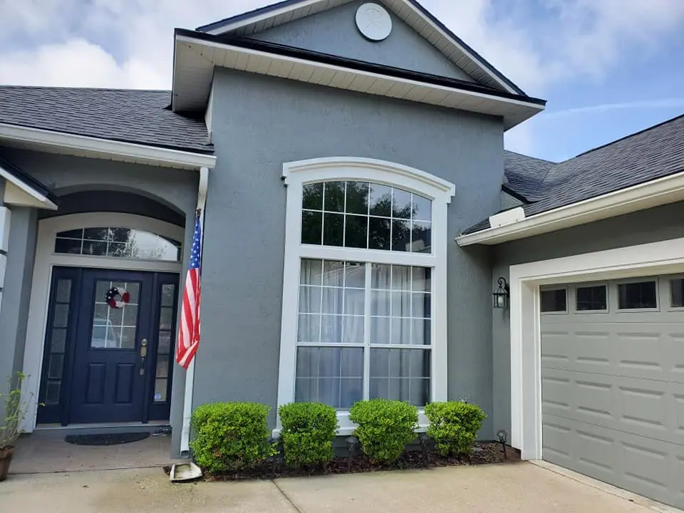 Gray stucco house front with a navy door and a flag